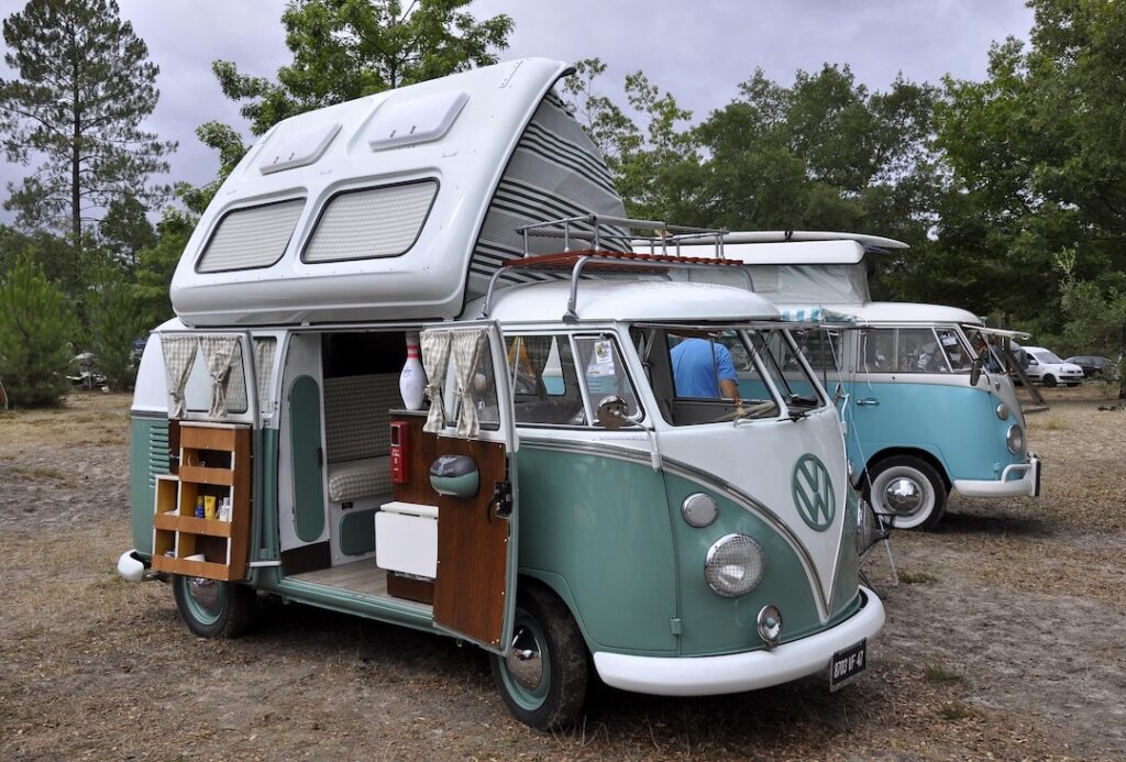 Volkswagen Transporter T1 camper cu plafon ridicat, alături de un alt T1 în natură